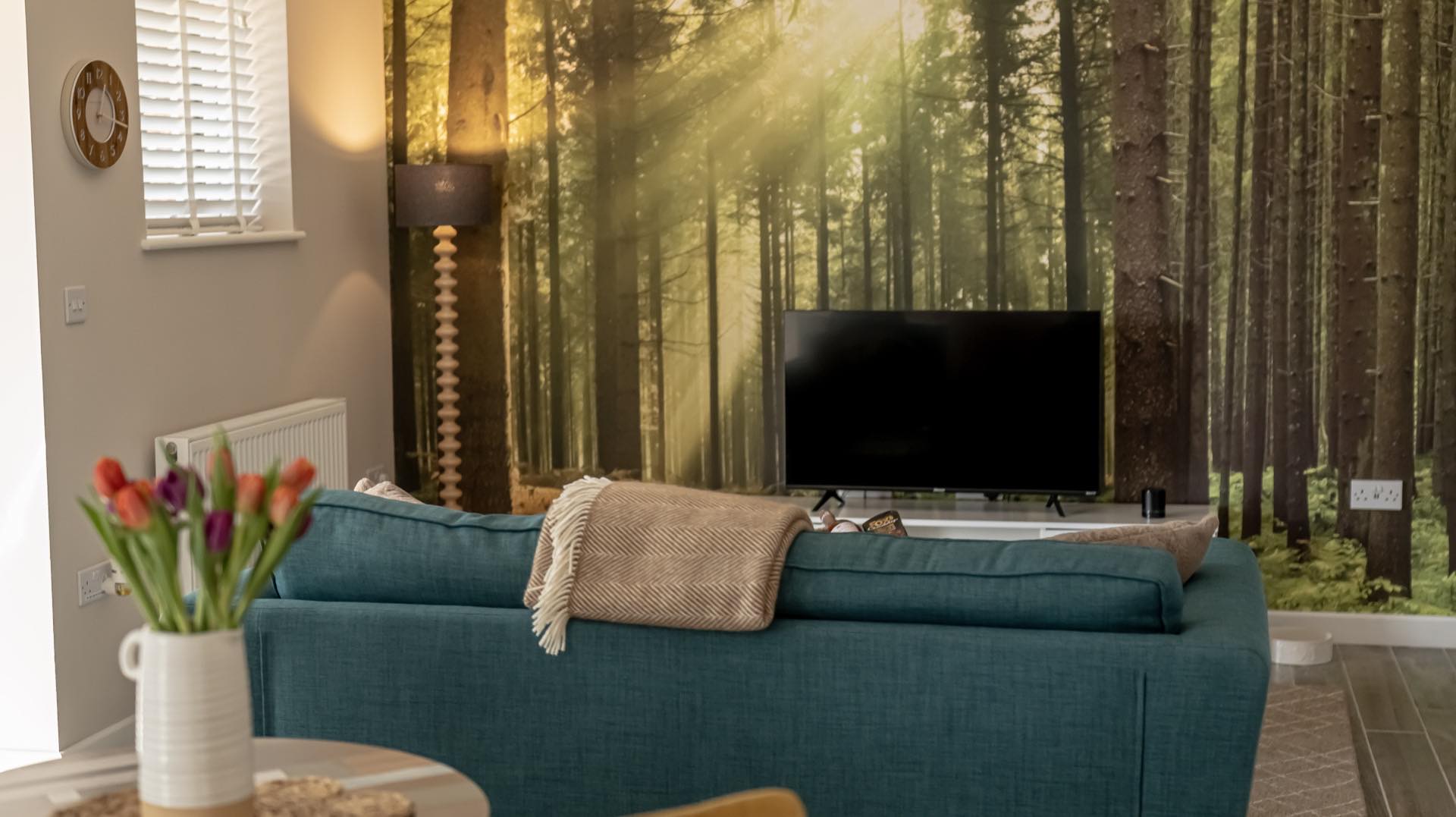 Elm living area with teal sofa, herringbone throw, flat-screen TV and a floor-to-ceiling forest mural wall