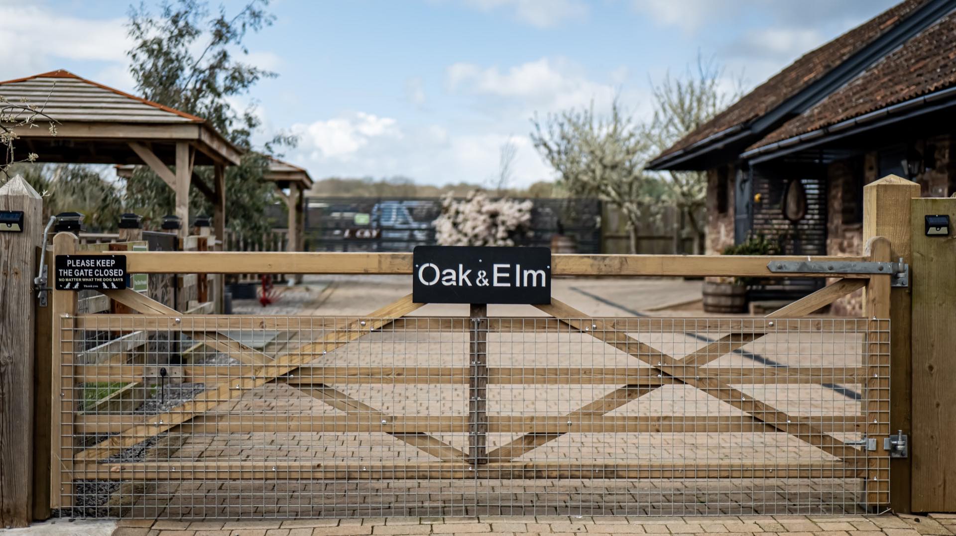 Wooden five-bar entrance gate with mesh infill and a please-keep-the-gate-closed notice, with a paved courtyard behind