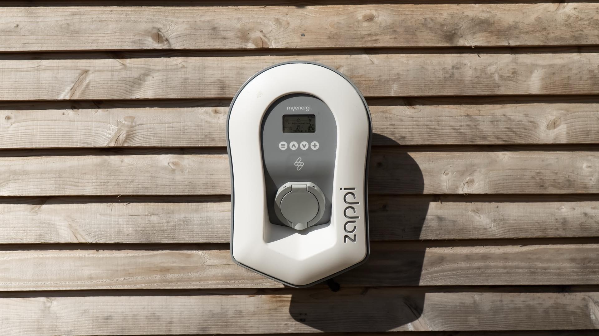 White zappi electric vehicle charging point mounted on timber cladding in sunshine