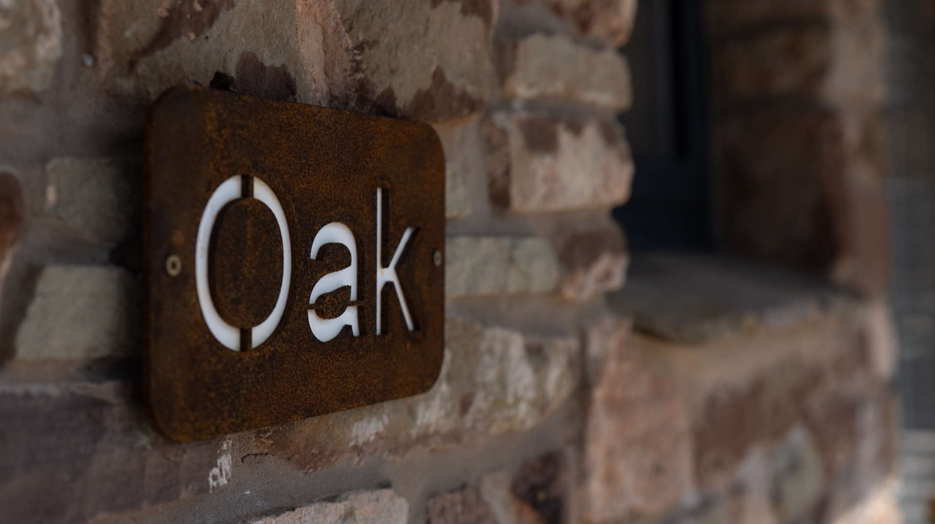 Close-up of a rusted metal name plate with cut-out lettering mounted on a stone wall