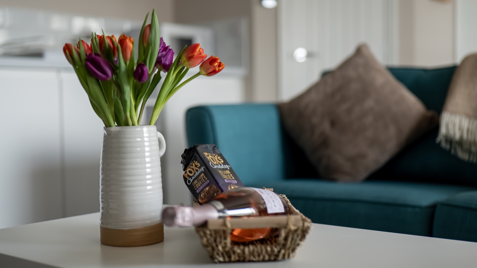 Welcome basket with a bottle of prosecco and cookies beside a jug of tulips on the Oak coffee table